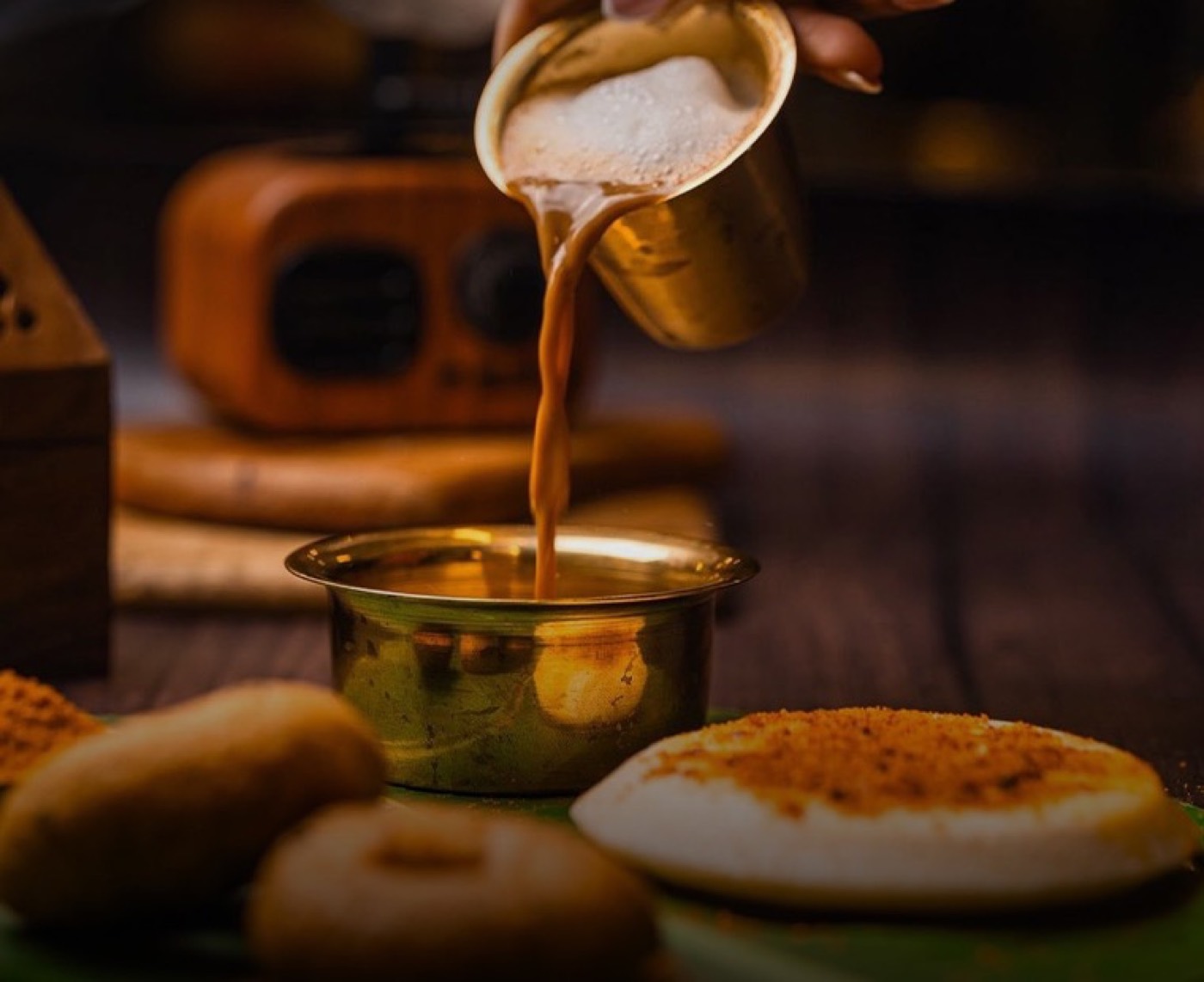 South Indian filter coffee poured from a brass tumbler beside idly and podi
